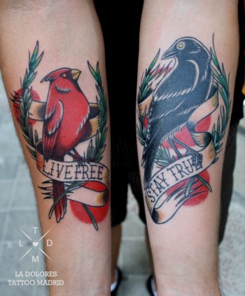 Tatuaje de dos pájaros, uno en cada antebrazo, posados en una corona de laurel