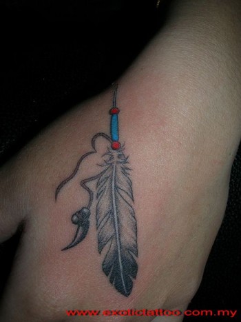 Tatuaje de una brazalete indio con una pluma y un colmillo colgando de la mano