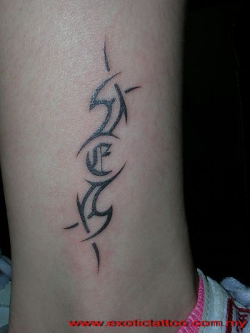Tatuaje de un pequeño tribal en la espinilla con una letra gótica dentro