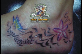 Tatuaje en el pie de una mariposa con una flor en el agua y varias letras tailandesas