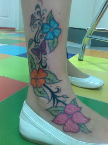 Enredadera con flores y mariposas tatuadas en el tobillo de una chica