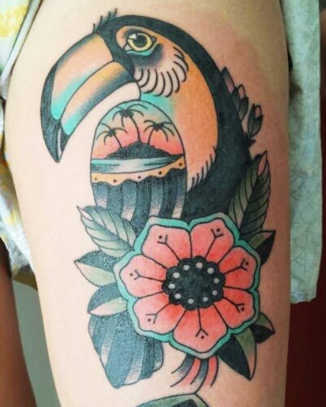 Tatuaje de un tucán en una flor, con un paisaje en su ala