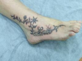 Tatuaje del nombre Laura entre algunas flores y planta