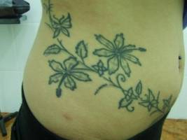 Tatuaje de una enredadera con flores por el costado de una chica