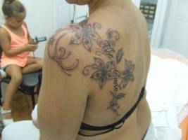 Tatuaje de enredaderas con flor cayendo por la espalda con un nombre dentro