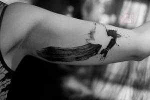 Tatuaje de un pájaro encima una linea hecha con pincel