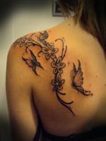 Tatuaje de una rama con flores y mariposas volando. Tatuaje para mujeres