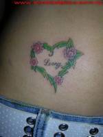 Tatuaje de un corazón formado por hojas y flores con un nombre dentro