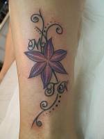 Tatuaje de una flor a color con varias lineas y unas iniciales