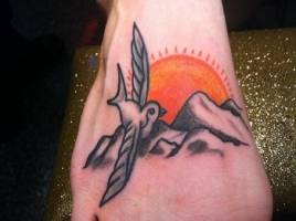 Tatuaje en el pie de pájaro volando sobre montañas