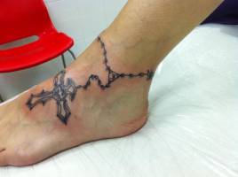 Tatuaje de una pulsera con una cruz tatuado en el pie