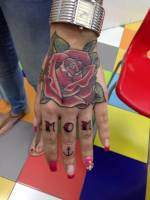 Tatuaje de una rosa en la mano, la palabra mom entre los dedos y un ancla
