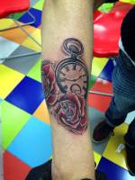 Tatuaje de unas rosas y un reloj en blanco y negro en el antebrazo