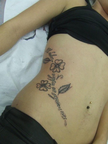 Tatuaje de unas flores en el costado, donde el tallo es una frase