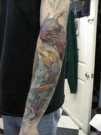Tatuaje de un ogro japonés en el brazo junto a una carpa koi 