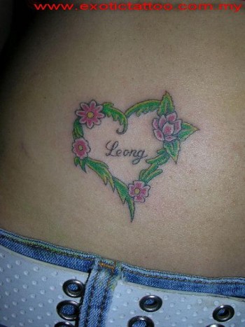 Tatuaje de un corazón formado por hojas y flores con un nombre dentro