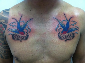 Tatuaje de dos golondrinas en el pecho con cintas para nombres