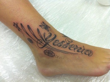 Tatuaje del nombre Yessenia con plantas flores y mariposas en el pie
