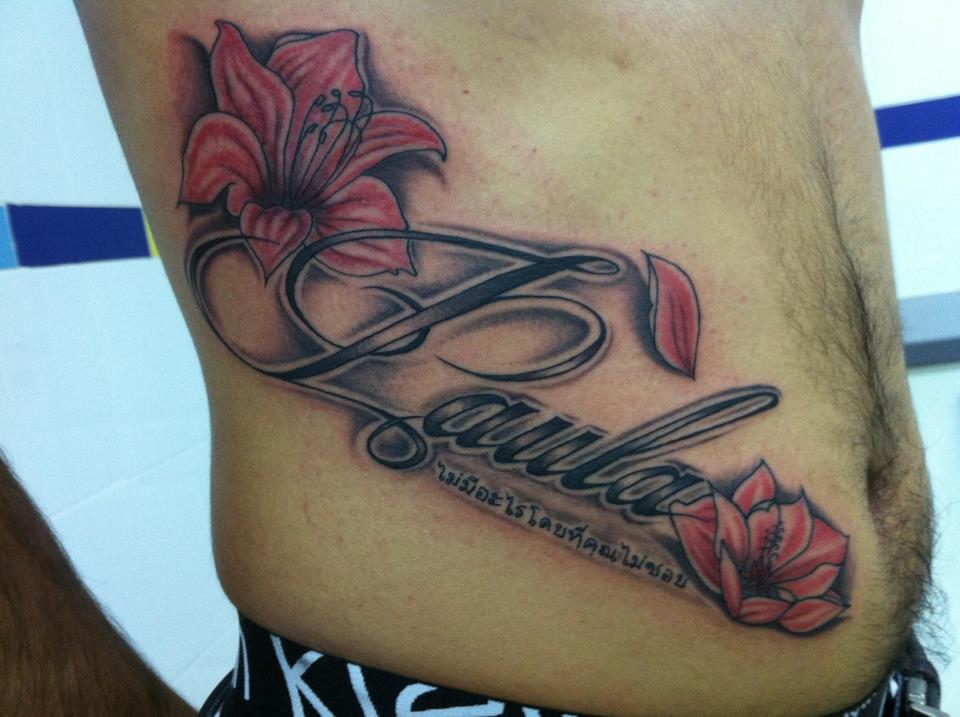 Tatuaje del nombre Paula con unas letras thai y un par de flores