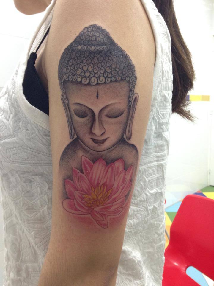 Tatuaje de una cara de buda y un loto a color en el brazo de una chica