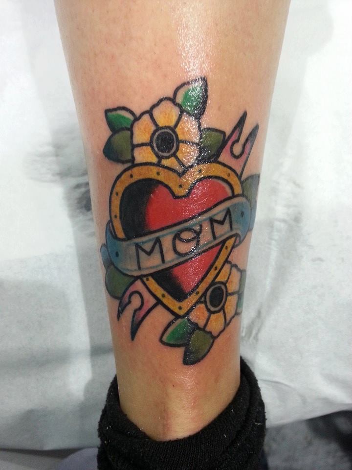 Tattoo a color de un corazón de hierro con una etiqueta y un par de florecitas