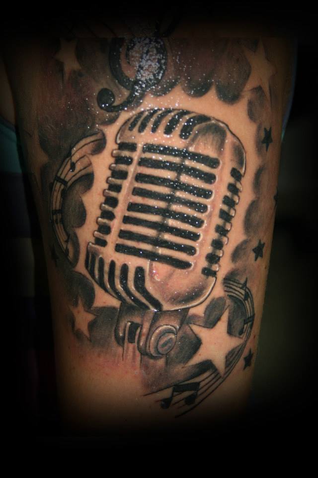 Tatuaje de un micrófono, estrellas y una partitura