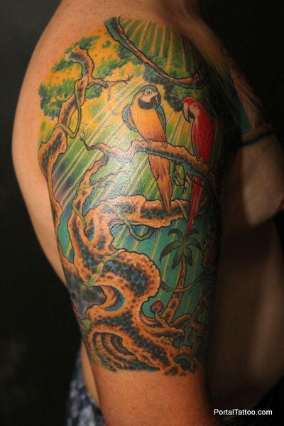 Tattoo de un bosque con loros en el brazo