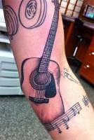 Tatuaje de una guitarra con una partitura debajo