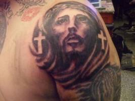 Tatuaje de la cabeza de cristo, entre dos cruces y unas manos rezando
