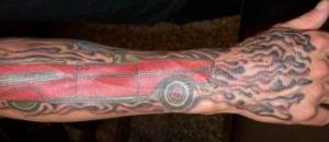 Tatuaje de un coche en el antebrazo y la mano en llamas