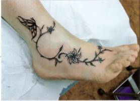 Tatuaje de una rama con una flor y mariposa en el pie