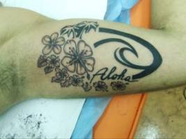 Tatuaje de unas flores, palmeras y una ola con la palabra Aloha