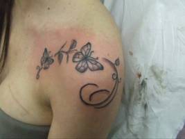 Tatuaje de unas mariposas y flores fnas en el hombro