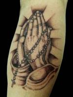 Tatuaje de unas manos rezando con un rosario colgando