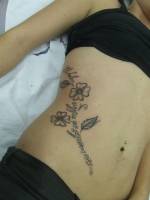 Tatuaje de unas flores en el costado, donde el tallo es una frase