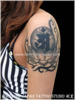Tatuaje de una flor de loto con una letra dentro y rodeado de tribales