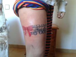 Tatuaje de un liguero con un nombre en la pierna de una mujer