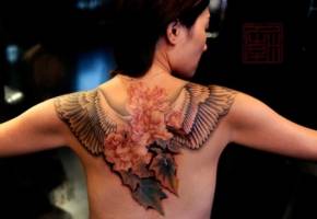 Tatuaje de unas flores con alas en la espalda de una mujer