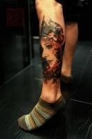 Tatuaje de una cara con kanjis en la pierna