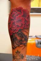 Tatuaje de calavera con flor y cruz en la pierna.