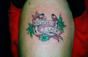 Tatuaje de una herradura con una etiqueta de suerte y un trébol