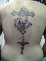 Tatuaje de unas manos rezando delante una cruz con un colgante de otra cruz