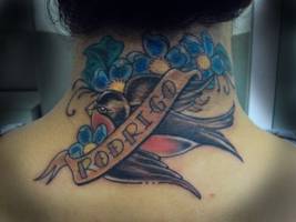 Tatuaje de una golondrina con flores llevando un nombre