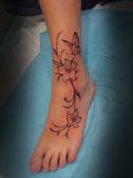 Tatuaje de unas flores con una mariposa en el tobillo