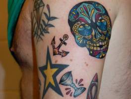 Tatuaje de una calavera mexicana, un ancla y una estrella entre varios objetos