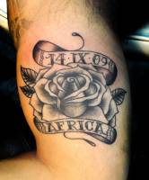 Tatuaje de una rosa con una etiqueta para fecha y otra para el nombre