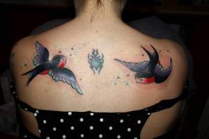 Tatuaje de golondrinas revoloteando en la espalda de una mujer