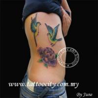Tatuaje de dos pájaros volando y una flor en el costado de una chica