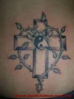 Tatuaje de una cruz entre ramas espinosas y con un yin yang dentro