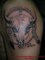 Tatuaje de una calavera de bisonte dentro de un circulo de madera con plumas colgando